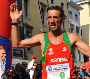 A distance runner, Paulo Pinheiro, raises his hand as crosses the finish line