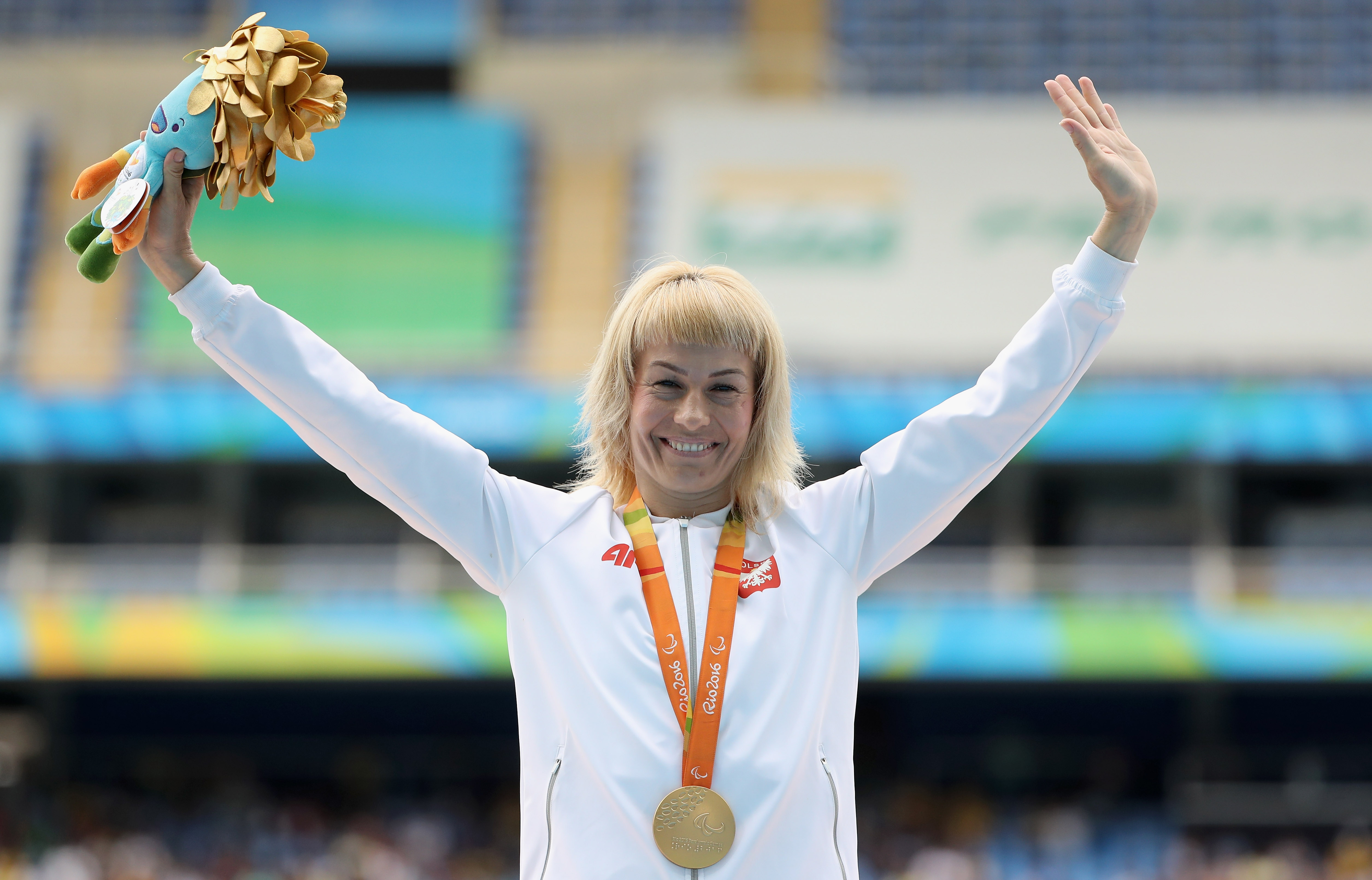 An athletes holds a mascot in the air whilst wearing a gold medal