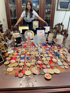 Women standing infront of table with more than 50 medals and trophies on display